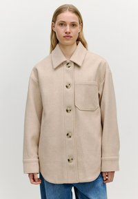 Beige Wollmischung Hemdjacke mit Spread-Kragen, Fronttasche und großen Knöpfen. Lockere Passform mit langen Ärmeln und umgeschlagenen Säumen.