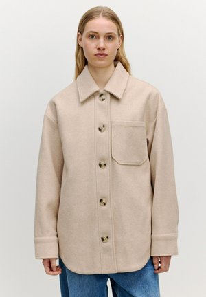 Beige wollen blend overhemdjasje met een spread collar, voorzak en grote knopen. Losse pasvorm met lange mouwen en omgeslagen manchetten.