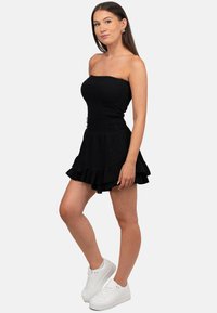 Zwarte strapless jurk met een smock-bloezend lijfje, ruffled zoom en lichtgewicht stof. Combinatie met witte sneakers voor een casual look.