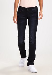 Mörkblå denimjeans med slim fit, som har subtila blekningar, fem fickor och knäppning. Matchas med vita sneakers.