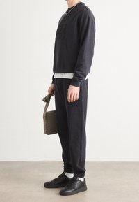 Sudadera marinera con el logo emblema "HUGO" en relieve, combinada con joggers a juego. Presenta puños acanalados y un tejido ligero. Zapatillas negras y un bolso color beige.