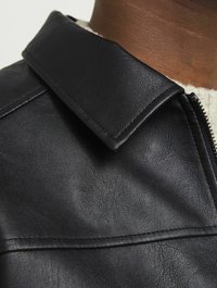 Chaqueta de cuero negra con un amplio cuello y superficie texturizada, con costuras visibles y un detalle de cremallera lateral.