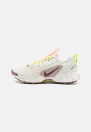 Chaussure de trail Nike, avec une tige en textile blanche ornée de motifs texturés, des accents marron, des lacets jaunes et une semelle en caoutchouc mouchetée.