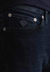 Mørke denim jeans med en glatt overflate, sølvfarge hardware og broderte logo-detaler på baklommen.
