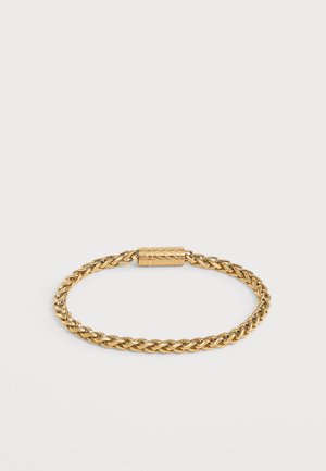 Bracelet chaîne torsadée ton or avec fermoir cylindrique présentant des motifs décoratifs gravés sur fond blanc uni.