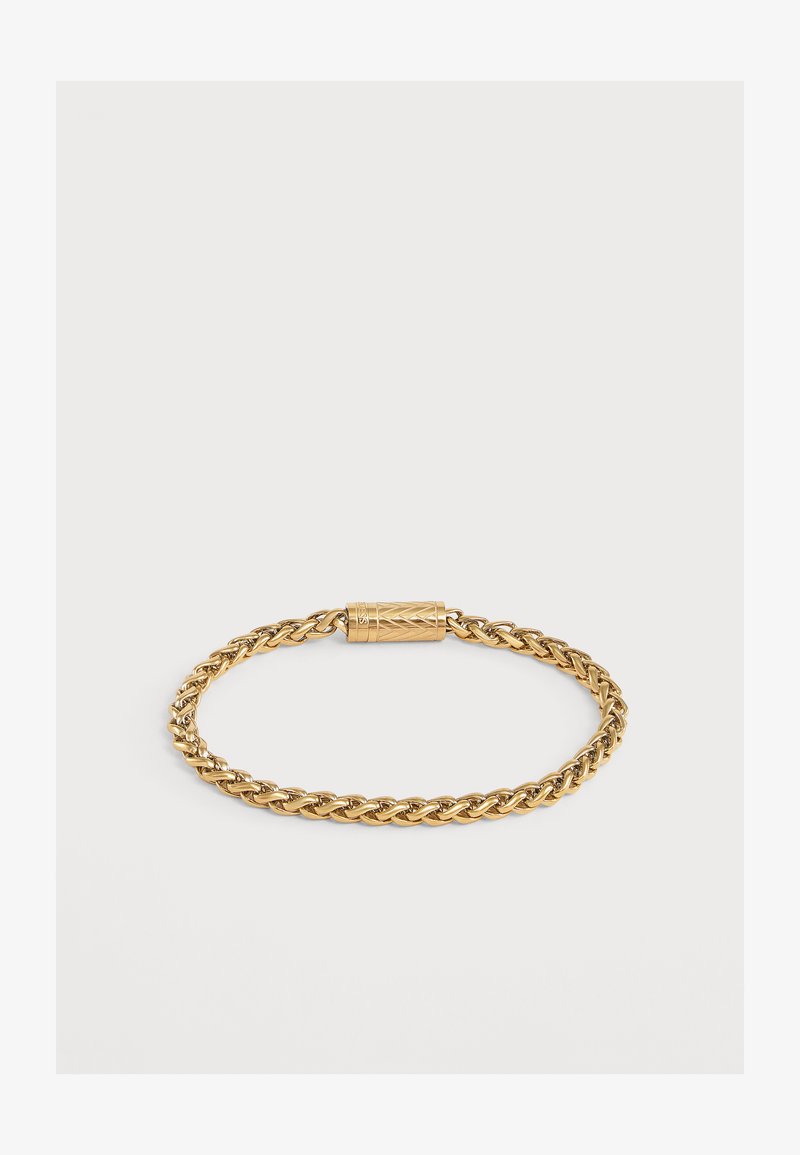 Bracelet chaîne torsadée ton or avec fermoir cylindrique présentant des motifs décoratifs gravés sur fond blanc uni.