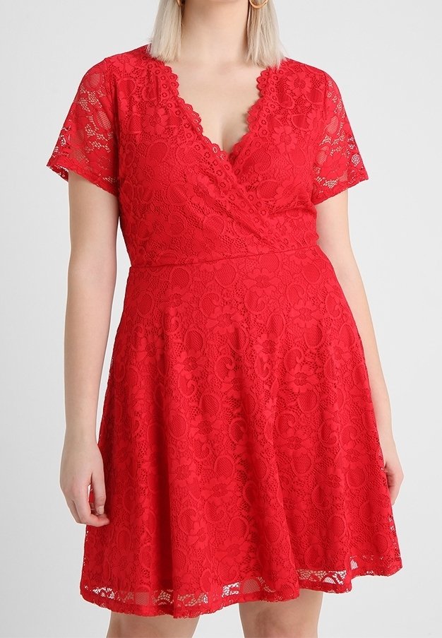 Kvinna klädd i en kortärmad klänning i röd spets med en vågig V-ringning och utsvängd kjol.