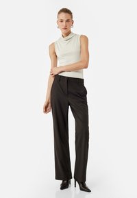 Sleeveless cowl-neck top in light beige. High-waisted, pinstriped dark trousers with straight legs. Black, pointed-toe heels.