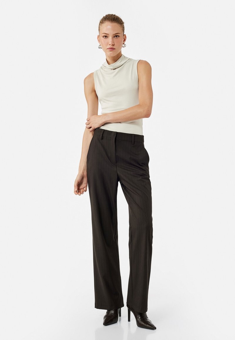 Sleeveless cowl-neck top in light beige. High-waisted, pinstriped dark trousers with straight legs. Black, pointed-toe heels.