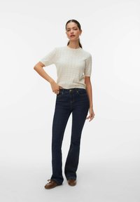 Helebeežist tekstuuriga kootud top lühikeste varrukatega, mida on kombineeritud tumedate siniste lõhenevate teksadega, millel on klassikaline nööpide sulgemine ja taskud.