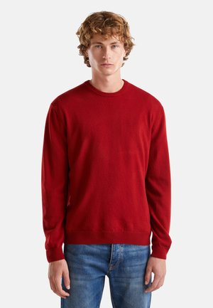 Roter Pullover aus einem weichen Stoff, mit Rundhalsausschnitt, langen Ärmeln und geripptem Saum und Bündchen, kombiniert mit blauen Jeans.