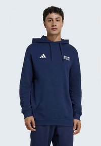 Marineblauwe hoodie van zachte stof. Voorzien van een kangoeroezak, een verstelbare trekkoordcapuchon en een wit Adidas-logo en tekst aan de voorkant.