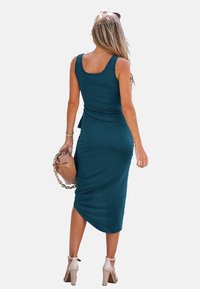 Teal bodycon šaty s výstřihem, na kterém je jemné nařasení v pase a délka ke kolenům. Spárováno s béžovou kabelkou a podpatky.