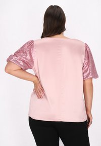 Lys pink bluse med korte, pailletbesatte puffærmer. Glat stof med en afslappet pasform, der har en rund halsudskæring og en ensfarvet ryg.