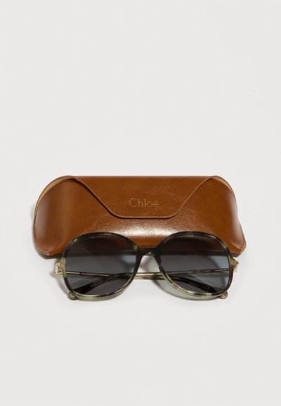 Καφέ δερμάτινη θήκη γυαλιών ηλίου Chloé με υπερμεγέθη γυαλιά ηλίου με σκούρους φακούς, που διαθέτουν λεπτούς μεταλλικούς βραχίονες τοποθετημένα μπροστά.