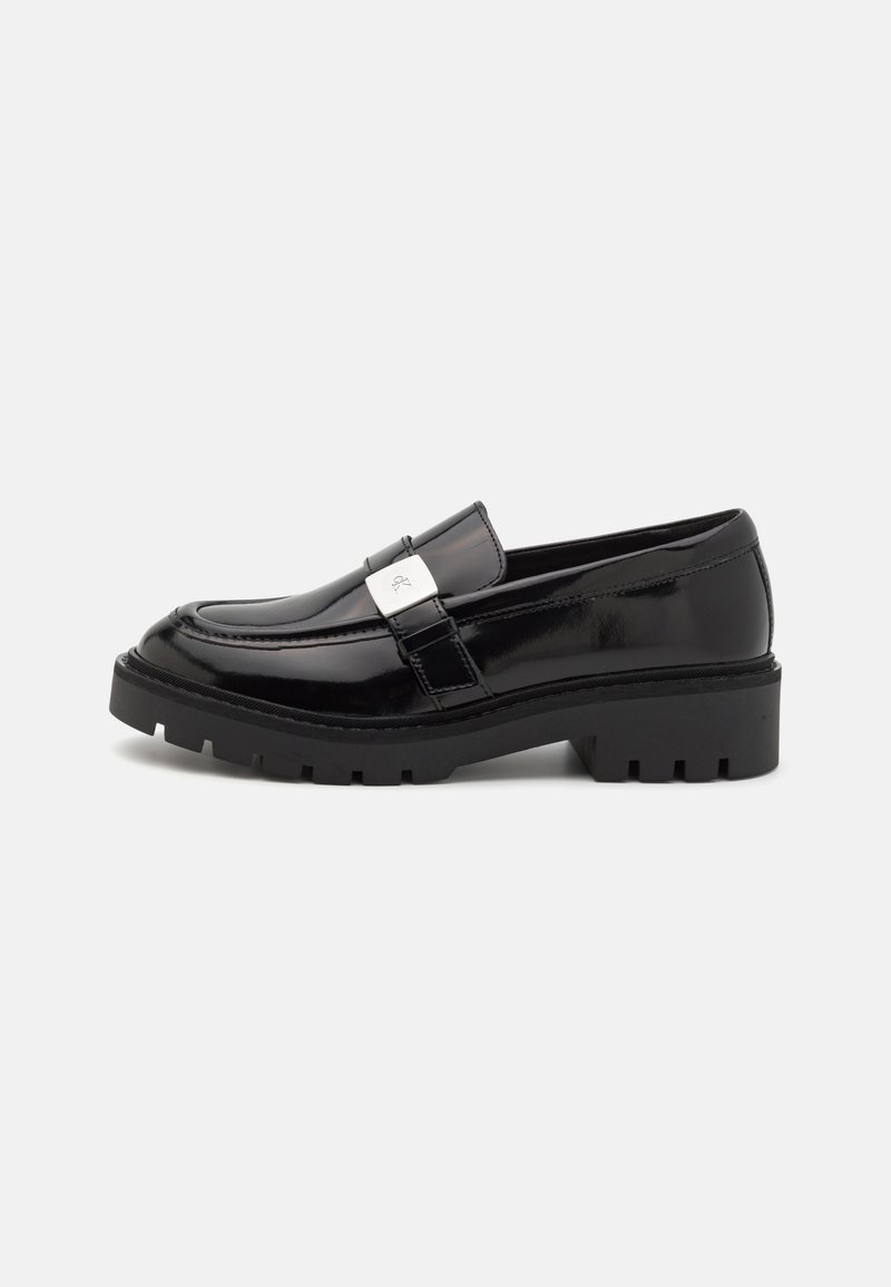 Schwarze Lackleder-Lederschuhe mit einer klobigen schwarzen Sohle, die einen metallischen Akzentriemen aufweisen. Runder Zehenbereich und strukturierte Oberfläche.
