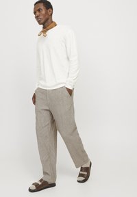 Camisa blanca de manga larga ligera, pantalones anchos de rayas beige y sandalias marrones con un diseño de tiras. Bufanda marrón alrededor del cuello.