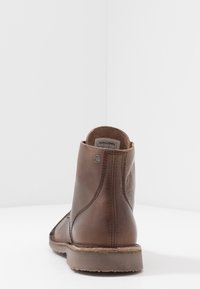 Hnědé kožené kotníkové boty s hladkým povrchem, kulatou špičkou a kontrastním šitím. Plná gumová podrážka a kovový detail loga na boku.