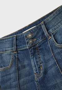 Dżinsy w ciemnoniebieskim kolorze, z wysokim stanem, dwoma metalowymi guzikami przy zapięciu oraz widocznymi detalami przeszyć wzdłuż szwów.