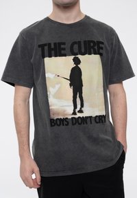 Gray cotton t-shirt featuring a front print of a silhouetted figure with a guitar, text "THE CURE" above and "BOYS DON'T CRY" below.