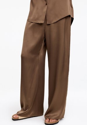 Braune Satin-Hose mit weitem Bein, kombiniert mit passendem Hemd und beigen offenen Sandalen mit Korksohlen.