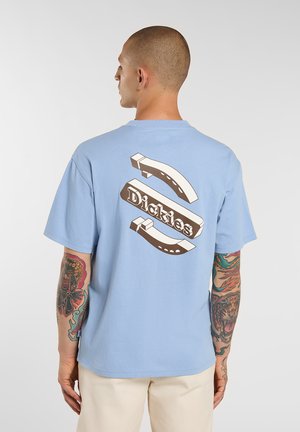 Camiseta de algodón azul claro con un gráfico audaz en marrón oscuro que incluye el texto "Dickies" y elementos estilizados en la parte trasera. Mangas cortas y corte holgado.