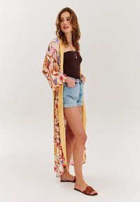 Kimono stylová róba s květinovými a abstraktními vzory, žluté lemování, lehká tkanina, kombinováno s hnědým topem a džínovými šortkami. Hnědé sandály.