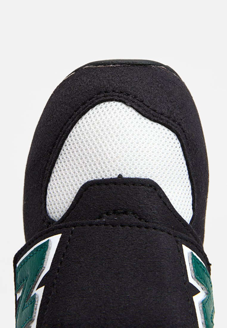 Bout de chaussure de sport en suédine noire avec une section en maille blanche, mettant en avant des accents verts et une surface texturée, des coutures surlignées et un logo bien visible.