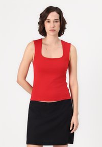 Top sin mangas rojo con escote cuadrado, hecho de un tejido suave y liso. Combinado con una falda negra, creando un look sencillo y contrastante.