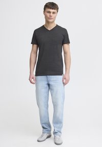 Camiseta negra de manga corta y escote en V combinada con jeans rectos de color azul claro y zapatillas grises, todo con fondo blanco plano.
