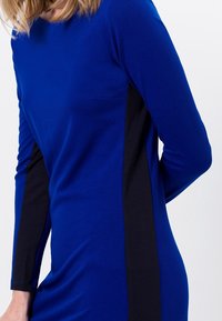 Abito a maniche lunghe con un vivace corpo principale blu, pannelli laterali neri e una forma aderente. Il materiale appare liscio con una leggera lucentezza.