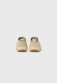 Pair of beige sneakers with suede and snake print accents shown from the back on a plain white background.