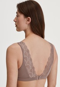 Bruine bralette met kantdetails op de rugbandjes, met een diepe V-vorm en een gladde textuur. Haaksluiting op de rug.