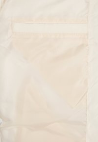 Poche intérieure en tissu beige avec une ouverture fendue horizontale sur une doublure de vêtement de couleur claire.
