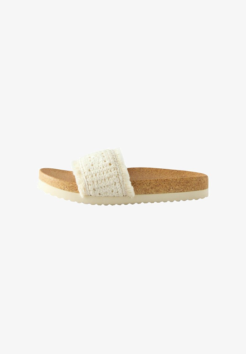 White woven fabric slide sandal with a cork sole and light rubber base, featuring fringe accents on the upper strap and a textured finish.