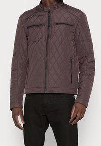 Gep quiltete dunkellila Jacke mit hohem Kragen, Reißverschluss vorne und zwei Brusttaschen. Verfügt über gerippte Akzente an den Ärmeln und dezente Markenkennzeichnung.