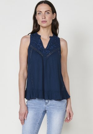 Marineblaue ärmellose Bluse mit gesticktem floralen Muster und gewelltem Ausschnitt. Mit gestuften Rüschen am Saum und strukturiertem Stoff.
