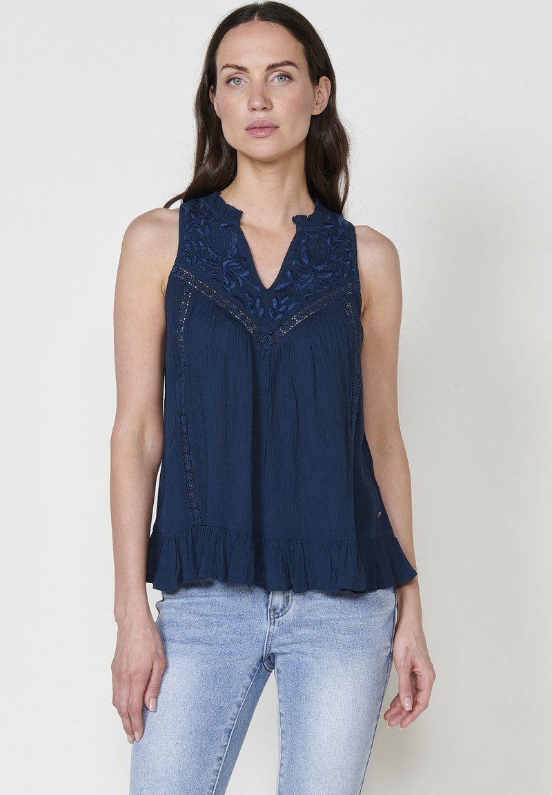 Top senza maniche blu navy con motivo floreale ricamato e scollatura ondulata. Presenta volant a strati all'orlo e tessuto testurizzato.