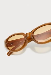 Bruna ovala solglas�ögon med genomskinliga bågar och gradientlinser. Har graverad logotyp och en slät, glänsande yta.