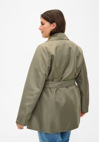 Khaki kabát se šněrováním a klopovým límcem, dlouhými rukávy a hladkým, matným povrchem. Má přiléhavý pas a uvolněný siluetu.