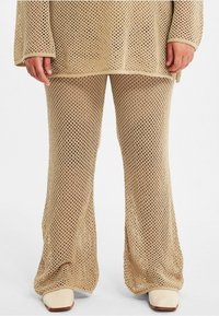 Beige stickad topp och utsvängda byxor har ett stort öppet nätmönster. Tyget visar textur, med lös väv och raka fållar.