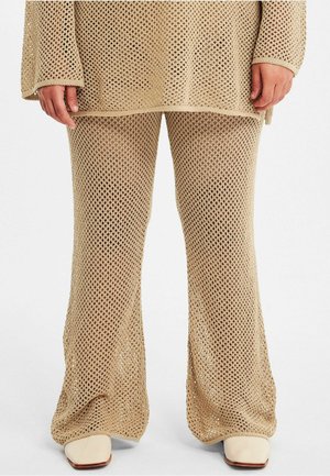 Beige gebreide top en uitlopende broek met een groot open gaaspatroon. De stof toont textuur, met een losse weef en rechte zomen.