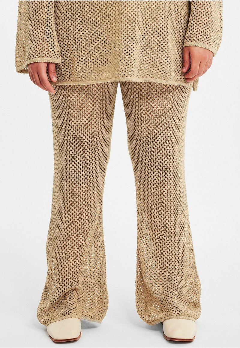 Beige stickad topp och utsvängda byxor har ett stort öppet nätmönster. Tyget visar textur, med lös väv och raka fållar.