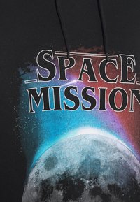 Sweat à capuche noir avec un graphique spatial coloré présentant la Terre et un texte blanc en gras « SPACE MISSION » au-dessus de la planète.
