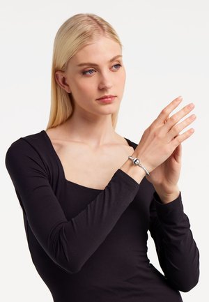Bracciale d'argento con un accento sferico liscio, indossato su una mano con pelle chiara. Il modello ha lunghi capelli biondi e indossa un top nero.