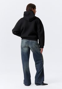 Schwarzer, übergroßer Kapuzenpullover mit Kapuze, kombiniert mit hellblauen Jeans mit entspannter Passform und dezentem Verblassen an den Knien.