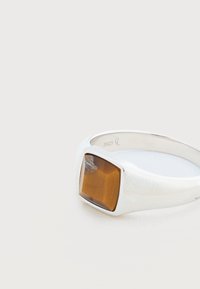 Anillo de plata con una piedra de ojo de tigre rectangular pulida, montada en una banda lisa, grabada con "S925" en el interior.