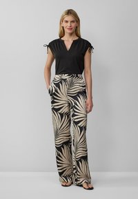 Top nero a maniche corte con scollatura a V, abbinato a pantaloni larghi beige con stampa di foglie di palma nere. Entrambi i capi sono leggeri.