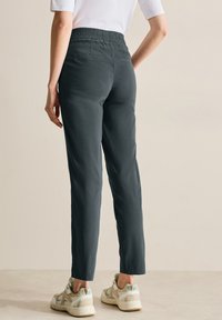 Mörkgrå byxor med elasticitet i midjan och tapered passform, två bakfickor och knälång skärning, i kombination med ljusa sportskor.