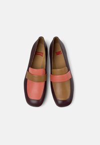 Läderloafers i burgundy, brunt och korall. Har ett brett band över ovandelen. Slät yta med rundad tådesign.